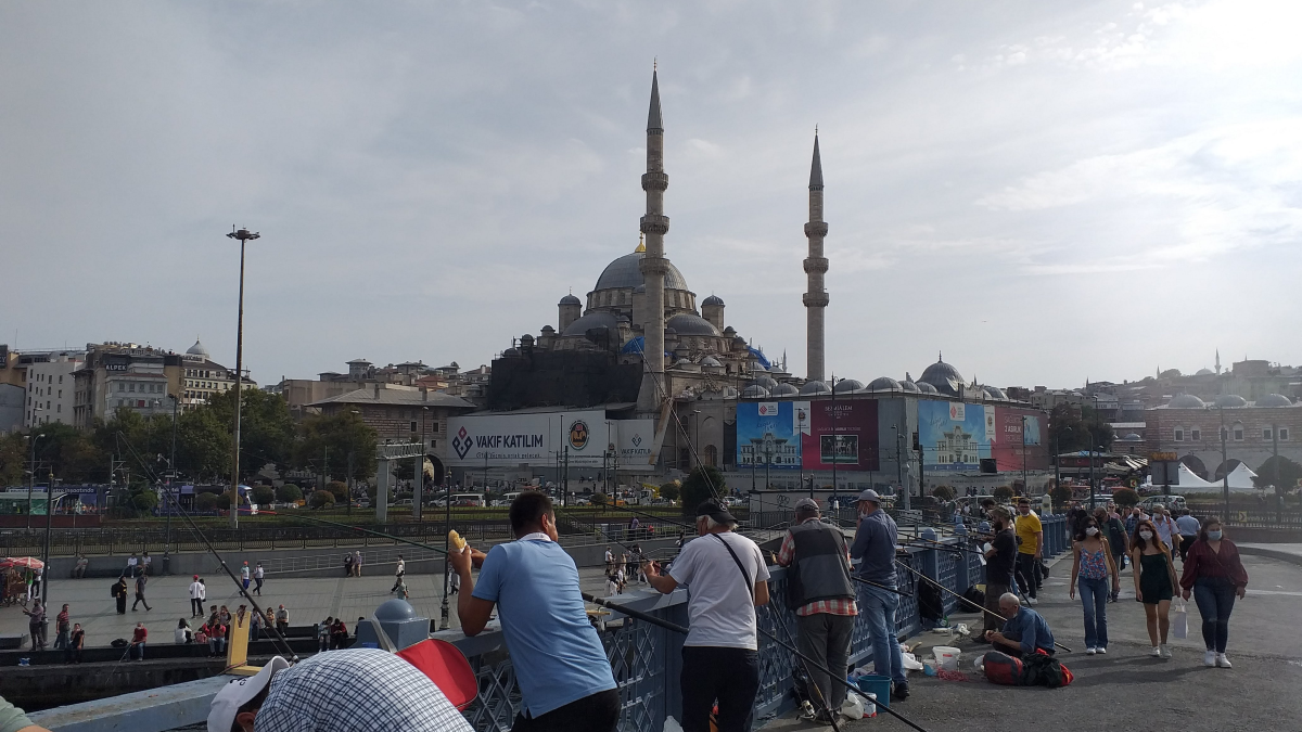 Anglers lining the Galata Bridge in Istanbul, with a grand mosque on the waterfront behind at Eminönü